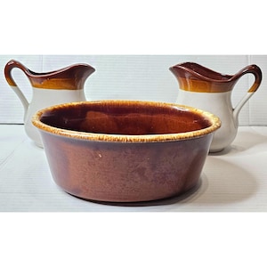 May include: A set of three brown and white glazed ceramic kitchenware pieces. The set includes a large bowl and two pitchers.