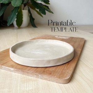 Può includere: Un vassoio in ceramica beige chiaro con un bordo leggermente arrotondato, appoggiato su un tagliere di legno. Il testo "Printable TEMPLATE" è visibile sopra il vassoio.