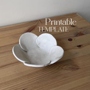 May include: A white, handmade, ceramic bowl in a flower shape. The bowl is sitting on a wooden surface. The text "Printable TEMPLATE" is in the background.