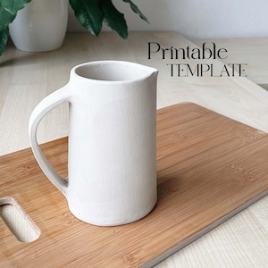 以下が含まれることがあります： 木製のまな板の上に置かれた、取っ手付きの白い陶器のピッチャー。背景には「Printable TEMPLATE」というテキストが表示されています。