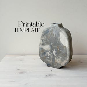 Pode incluir: Um vaso de cerâmica cinza e branco com um design de mármore. O vaso tem uma forma arredondada, orgânica e uma abertura larga.