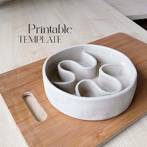 May include: A white ceramic slow feeder bowl with a maze design. The bowl is on a wooden cutting board. The text "Printable TEMPLATE" is above the bowl.