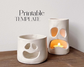 May include: Two white ceramic ghost candle holders with cut-out faces. The larger ghost has a sad face and a lit candle inside. The smaller ghost has a happy face. The candle holders are on a wooden surface. Printable TEMPLATE text is at the top of the image.