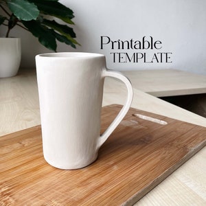 May include: A white ceramic mug with a handle. The mug is sitting on a wooden chopping board. The text "Printable TEMPLATE" is visible in the background.