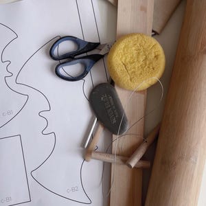 May include: A craft project with a variety of materials including a paper template, scissors, a yellow sponge, a black stone, a metal rod, and wooden dowels.