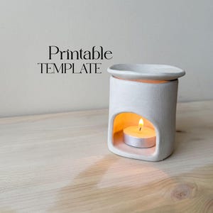 May include: A white ceramic essential oil diffuser with a lit tea light candle inside. The diffuser has a rectangular shape with a curved top and a rounded opening. The text "Printable TEMPLATE" is above the diffuser.