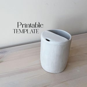 May include: White ceramic planter with a divided top, perfect for small plants or succulents. The planter has a simple, modern design and is ideal for adding a touch of greenery to any space. Printable TEMPLATE text is visible in the image.