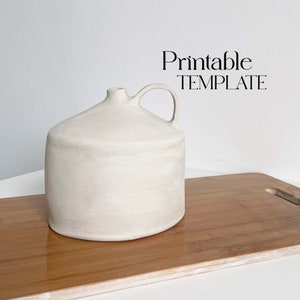 Puede incluir: Una jarra de cerámica blanca con asa, sentada sobre una superficie de madera. La jarra tiene un cuerpo redondeado y un labio ligeramente acampanado.  Printable TEMPLATE.