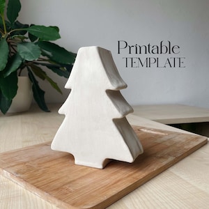 Könnte beinhalten: Ein weißer Keramik-Weihnachtsbaumschmuck mit einfachem Design. Der Schmuck liegt auf einem Holzbrett. Druckbarer TEMPLATE.