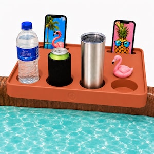 May include: A terracotta-colored rectangular pool side tray with multiple slots for beverages and mobile devices. It holds a clear plastic water bottle, a black can cooler, a stainless steel tumbler, two smartphones, and a small pink flamingo toy.