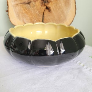 May include: A black and yellow ceramic bowl with a scalloped rim. The bowl is shaped like a pumpkin.