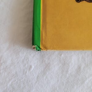 May include: A yellow book with a green spine. The book is slightly worn and has a small tear on the bottom edge.