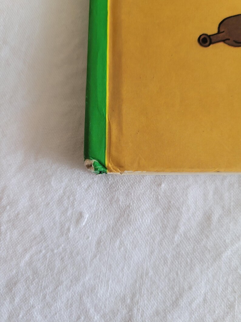 May include: A yellow book with a green spine. The book is slightly worn and has a small tear on the bottom edge.