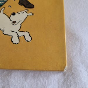 May include: A yellow book cover with a white dog running towards the right side of the page. The dog has black eyes and a black nose. The dog is on a yellow background with a few white dots.
