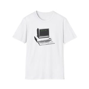 May include: White t-shirt featuring a black and white graphic of an old computer with the text "wake up, Neo." The design includes a monitor, keyboard, and the text in green. The shirt is a classic crew neck.