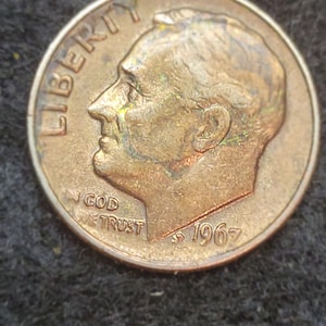 May include: A copper-colored 1967 United States dime coin with the words "Liberty", "In God We Trust", and the year "1967" inscribed on it. The coin features a profile of President Franklin D. Roosevelt.