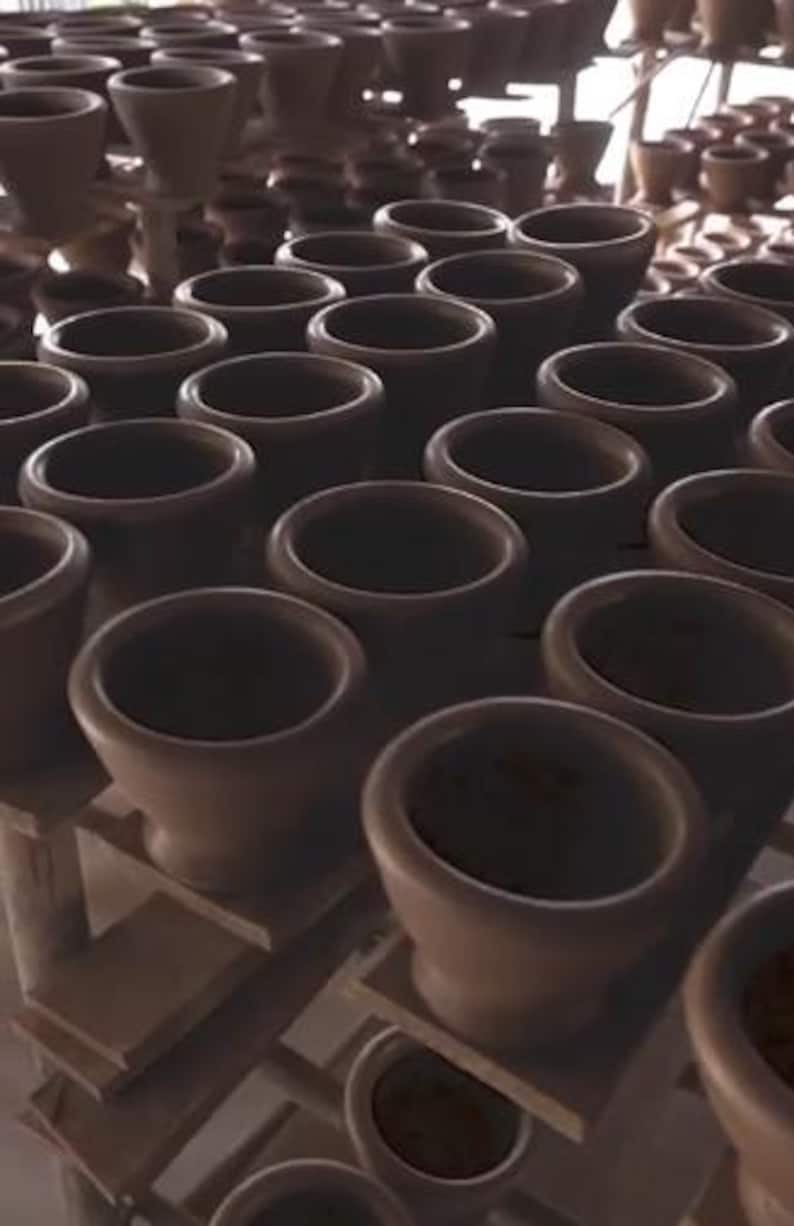 May include: A collection of brown ceramic mortar and pestle sets, arranged on wooden shelves. The mortars have a wide, open bowl shape, and the pestles are not visible. The lighting is soft, highlighting the texture of the pottery.