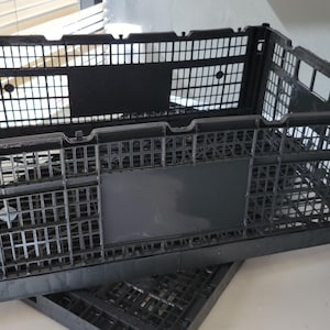 May include: A black plastic folding crate with a grid pattern. The crate is empty and has a flat bottom.