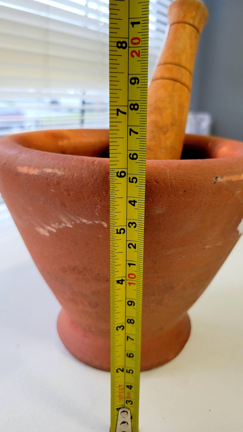 May include: A terracotta mortar and pestle set. The mortar is approximately 8 inches tall. The pestle is made of wood. The mortar has a wide opening and a tapered body. The set is designed for grinding and mixing ingredients.