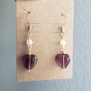 May include: A pair of purple heart-shaped dangle earrings with a small pink bead on each earring.