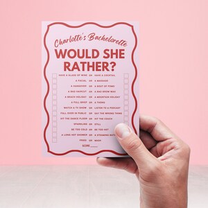 May include: A pink card with the text "Charlotte's Bachelorette Would She Rather?" and a list of questions with checkboxes. The card is held in a hand.