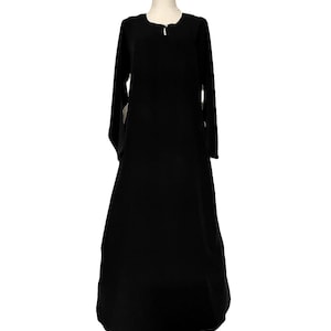 May include: A long, black dress with long sleeves and a round neckline. The dress has a simple, elegant design and a flowing silhouette. The dress is displayed on a mannequin.