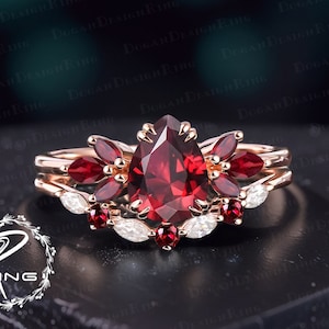 Peut inclure: Une bague de fiançailles en or rose sertie d'une pierre précieuse rouge en forme de poire entourée de petites pierres précieuses rouges et d'une bande de diamants blancs.