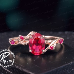 Könnte beinhalten: Ein Ring aus Roségold mit einem großen ovalen Rubin-Edelstein und kleineren Rubin-Akzenten. Die Band ist verdreht und hat ein Blattdesign.