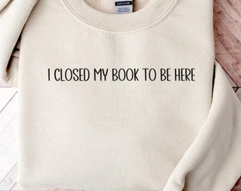 May include: A beige sweatshirt with the text "I closed my book to be here" printed on the front.