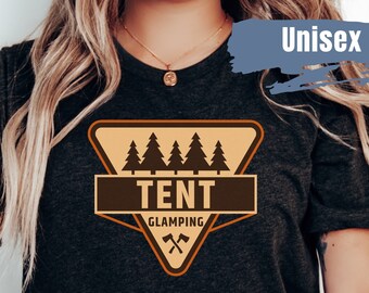 Puede incluir: Una camiseta gris oscuro con un gráfico triangular marrón y naranja. El gráfico presenta una línea de pinos, la palabra "TENT" y las palabras "GLAMPING" con dos hachas cruzadas.