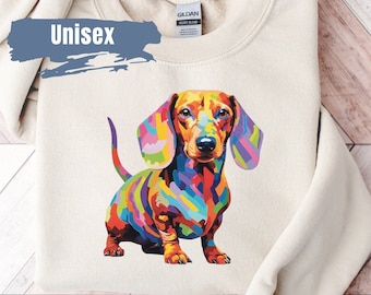 Op de afbeelding: Een beige sweatshirt met het woord "Unisex" gedrukt op de linkerzijde van de borst. Een kleurrijke teckel is gedrukt op de rechterzijde van de borst.