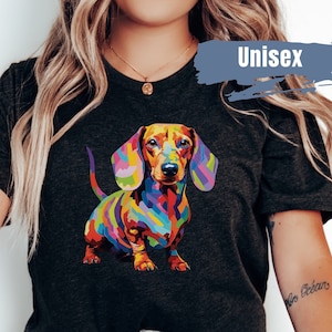 May include: A dark grey t-shirt featuring a colourful dachshund graphic. The dachshund is depicted in a pop art style with bright colours and bold lines. The shirt is unisex and has a crew neck.