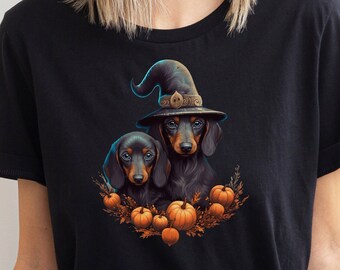 Op de afbeelding: Zwart T-shirt met een Halloween-illustratie. Het ontwerp toont twee teckels, waarvan één met een heksenhoed, omringd door pompoenen en herfstbladeren. De illustratie is kleurrijk en gedetailleerd, perfect voor het griezelige seizoen.