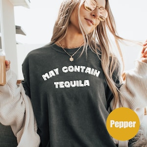 Puede incluir: Sudadera gris oscuro con el texto blanco "MAY CONTAIN TEQUILA". La palabra "Pepper" está en un círculo amarillo en la esquina inferior derecha. La sudadera es de estilo casual.