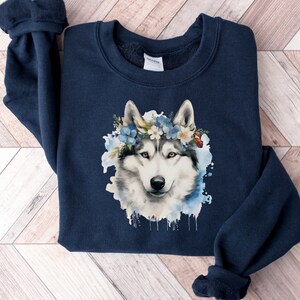 Op de afbeelding: Marineblauw sweatshirt met een aquarel illustratie van een husky hond met een bloemenkrans. De hond heeft wit en grijs haar, met blauwe en witte bloemen in de krans. Het sweatshirt is gemaakt van zacht materiaal.