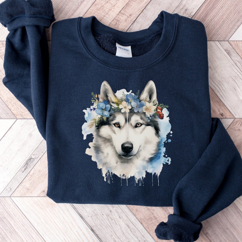 Op de afbeelding: Marineblauw sweatshirt met een aquarel illustratie van een husky hond met een bloemenkrans. De hond heeft wit en grijs haar, met blauwe en witte bloemen in de krans. Het sweatshirt is gemaakt van zacht materiaal.