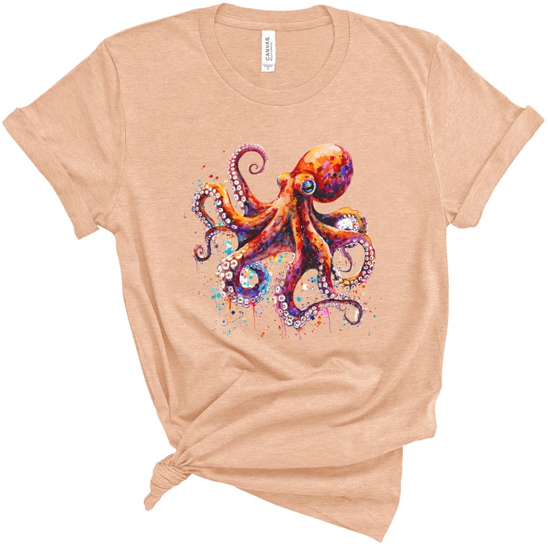 Puede incluir: Una camiseta de color melocot&oacute;n claro con una ilustraci&oacute;n de acuarela de un pulpo con tent&aacute;culos coloridos y una salpicadura de pintura alrededor.