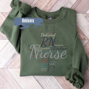 May include: A green unisex sweatshirt with a graphic design of the word "Nurse" in a word cloud style. The word cloud is made up of words that describe the qualities of a nurse, such as "caring", "dedicated", "empathic", and "resilient".