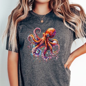 Puede incluir: Una camiseta gris oscuro con una ilustraci&oacute;n colorida de un pulpo. El pulpo est&aacute; pintado en tonos de rojo, naranja, rosa y morado con salpicaduras de pintura azul y amarilla.