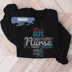 May include: Black sweatshirt with a word cloud design featuring the words "RN" and "Nurse" in a colorful font. The words are surrounded by other words describing the qualities of a nurse, such as "compassionate", "skilled", and "dedicated".