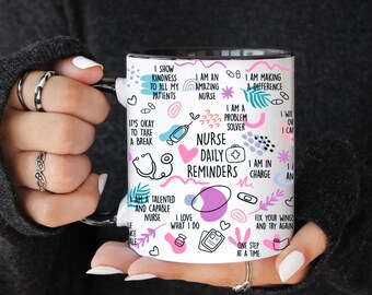 May include: A white ceramic mug with a black interior and handle, featuring the text "Nurse Daily Reminders" and various related illustrations in blue, pink, and purple. The mug is held by a person.