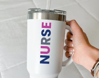 May include: White insulated tumbler with a silver rim and handle. The word "NURSE" is printed vertically in pink and navy blue. The tumbler is designed to keep beverages hot or cold.