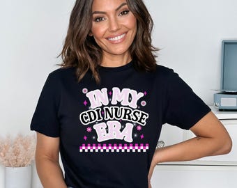 May include: Black t-shirt with the text "IN MY CDI NURSE BRA" in pink and white, with decorative elements. The shirt is short-sleeved and has a crew neck.