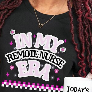 May include: Black t-shirt with the text "IN MY REMOTE NURSE ERA" in white and pink. The shirt also features daisy and star graphics. A white mug with the text "TODAY'S Good Mood IS SPONSORED BY Coffee" is visible.