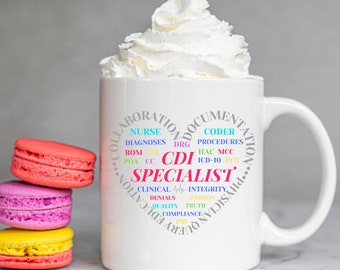 May include: A white ceramic mug with a heart-shaped design filled with medical terms, including "CDI Specialist." The mug is topped with whipped cream. Three colorful macarons are stacked to the left of the mug.