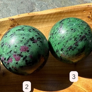 May include: Four green and pink gemstone spheres arranged in a row on a wooden tray. The spheres are numbered 1 through 4.