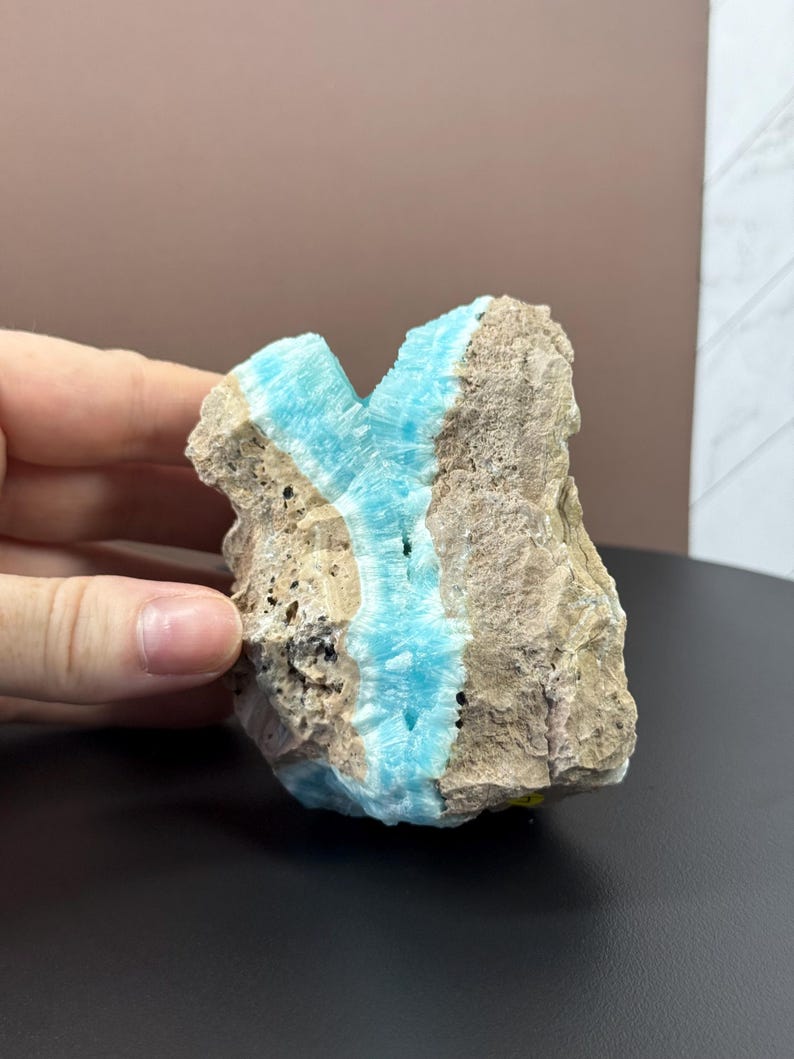 May include: A rough, natural stone with a striking vein of bright turquoise blue running through it. The stone's exterior is a mix of beige and brown, with a textured surface. The blue vein adds a vibrant contrast to the earthy tones of the rock.
