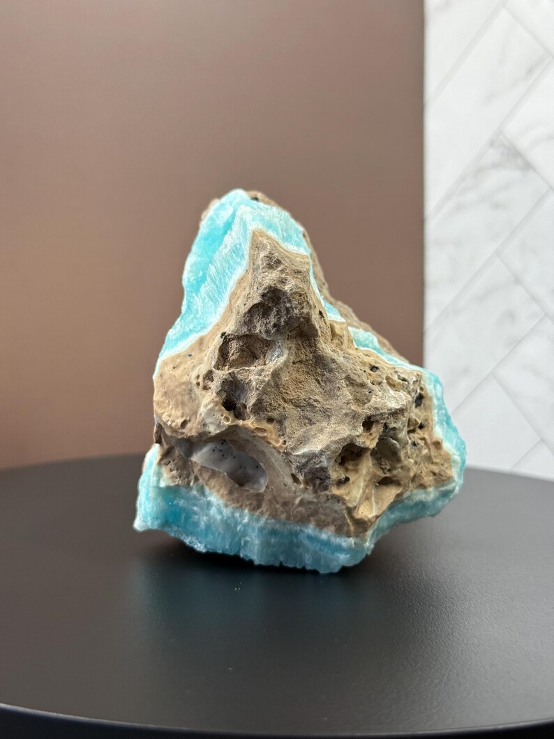 May include: A rough-hewn, natural stone specimen featuring a striking contrast of colors. The stone displays a vibrant turquoise hue along its edges, juxtaposed against a textured, earthy brown and gray core. The mineral sits on a black surface.