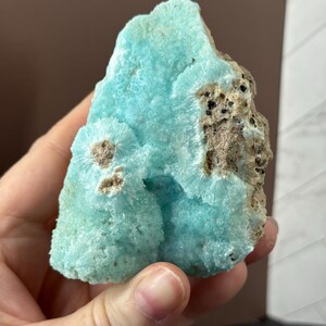 Puede incluir: Un vibrante esp&eacute;cimen mineral en bruto con un llamativo tono turquesa. La piedra presenta una superficie texturizada con formaciones cristalinas e inclusiones marrones y negras. Esta pieza &uacute;nica es una gema natural sin pulir.
