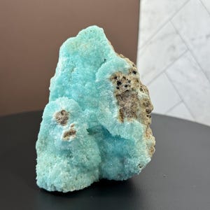 Puede incluir: Impresionante esp&eacute;cimen mineral natural con una vibrante estructura cristalina azul claro. El mineral tiene una superficie rugosa y texturizada con &aacute;reas de color marr&oacute;n y beige. La forma general es irregular y org&aacute;nica, mostrando la belleza de las formaciones naturales.